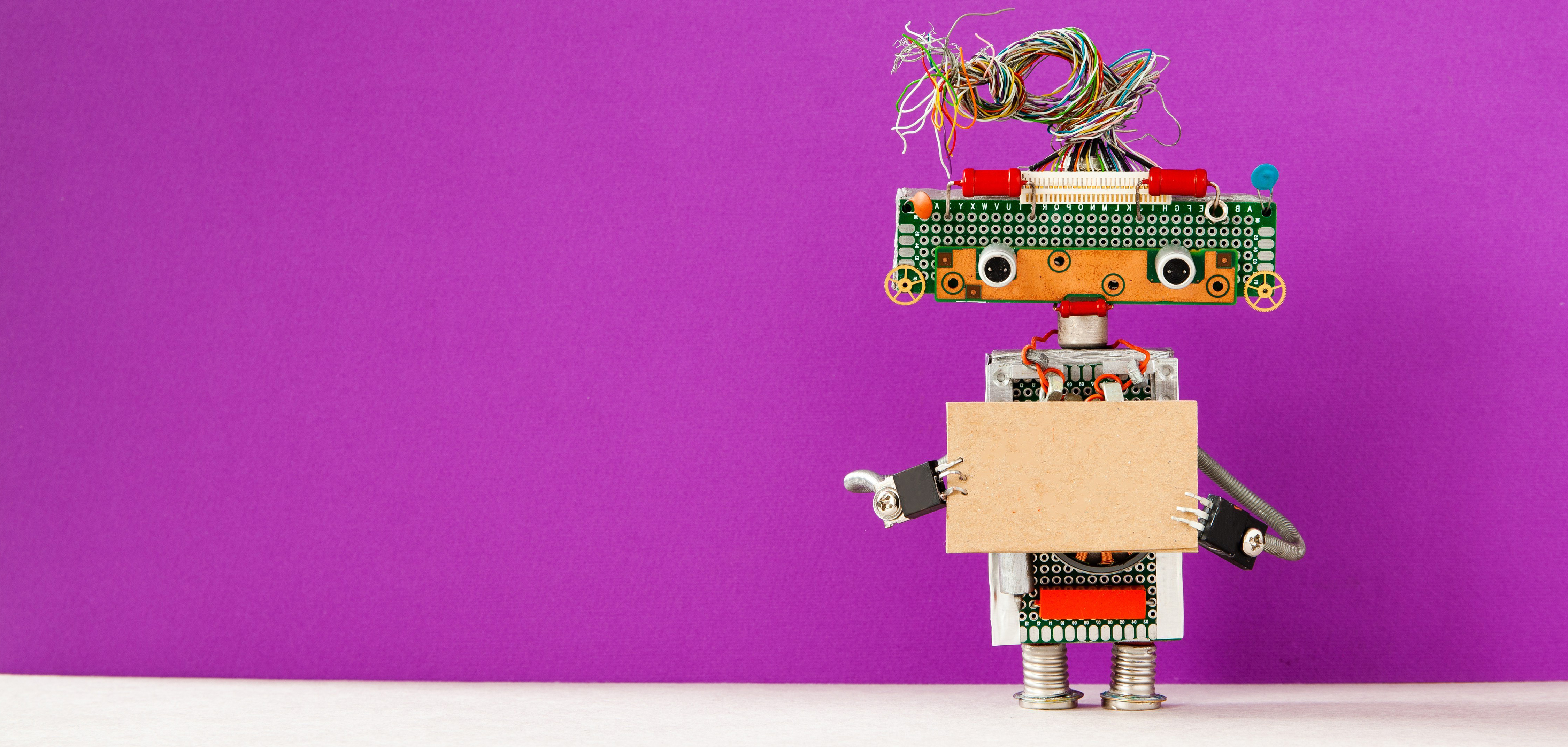 Robot with a cardboard card mockup. Creative design robotic toy holding a blank empty paper poster, purple wall background. Programs for Scouts - Girl Scouts Robotics Workshop